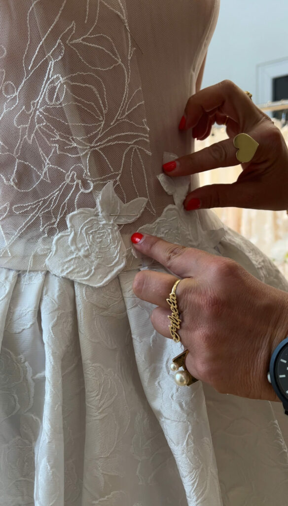 Red-polished hands adjust lace on modern wedding dress.