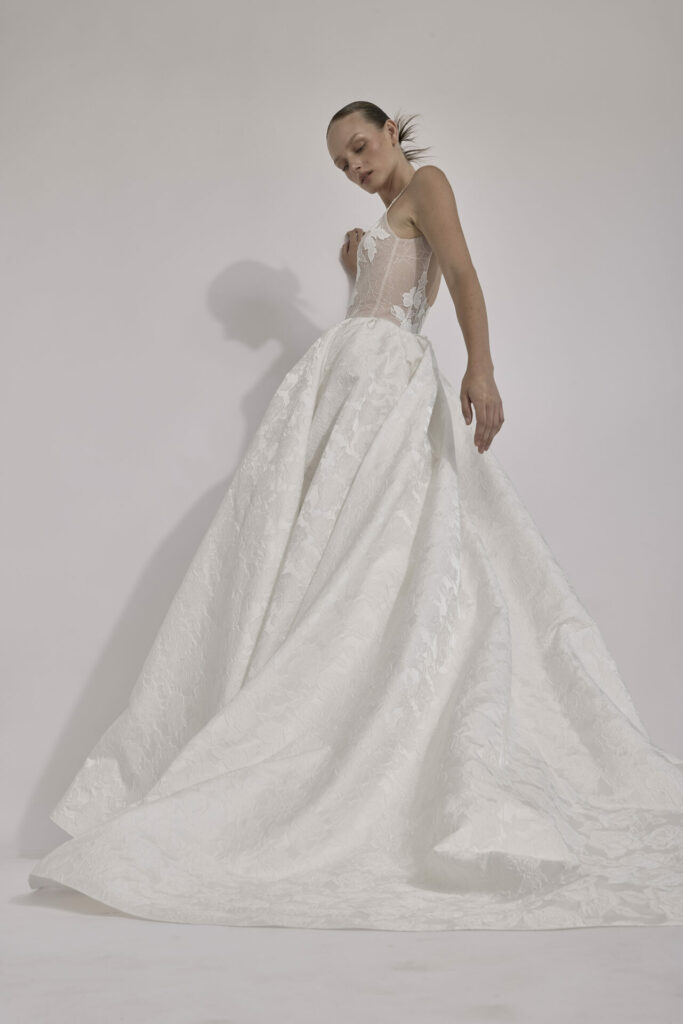 Woman in sheer corset gown looks down, posing.