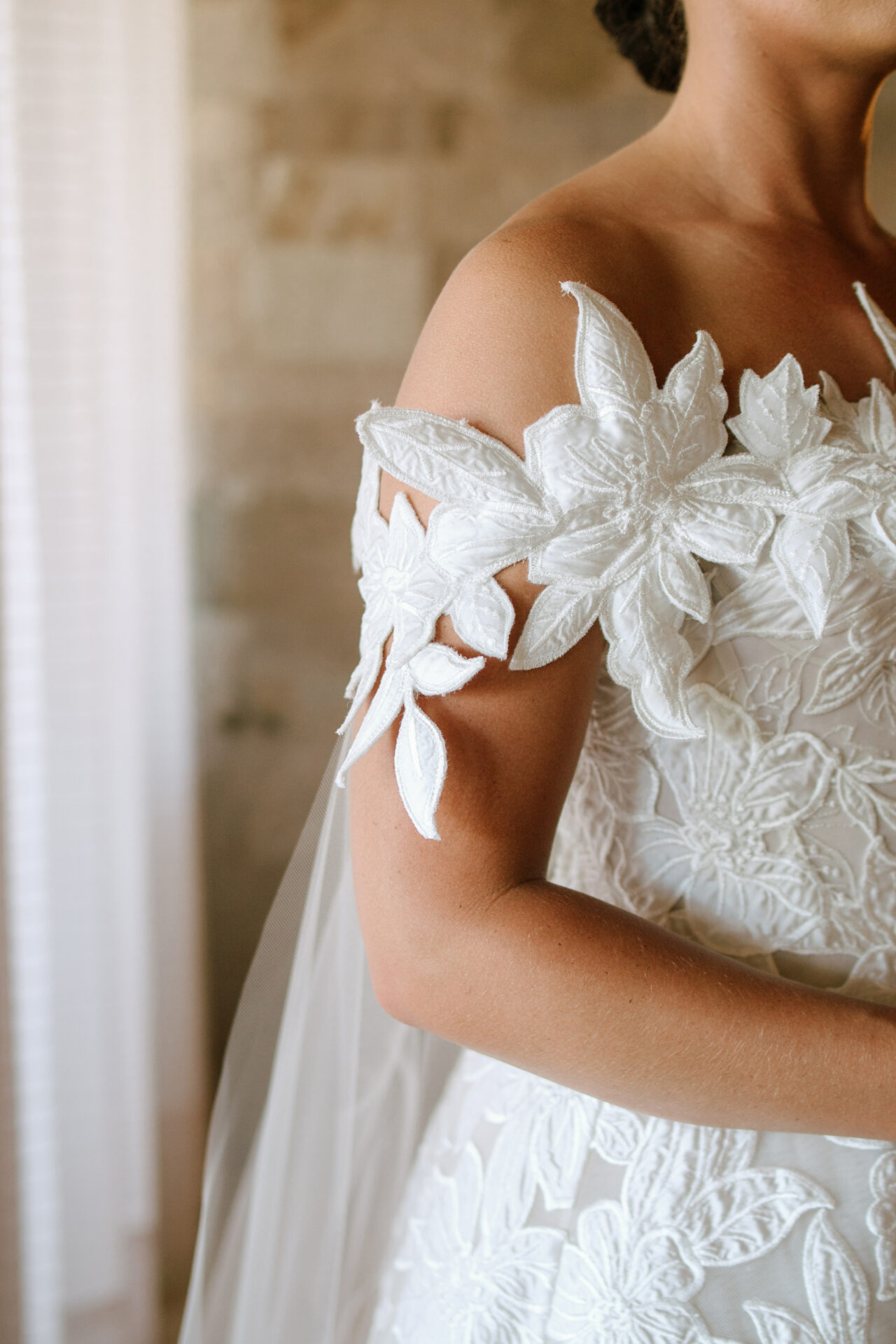 Woman in floral lace off-shoulder wedding dress indoors.