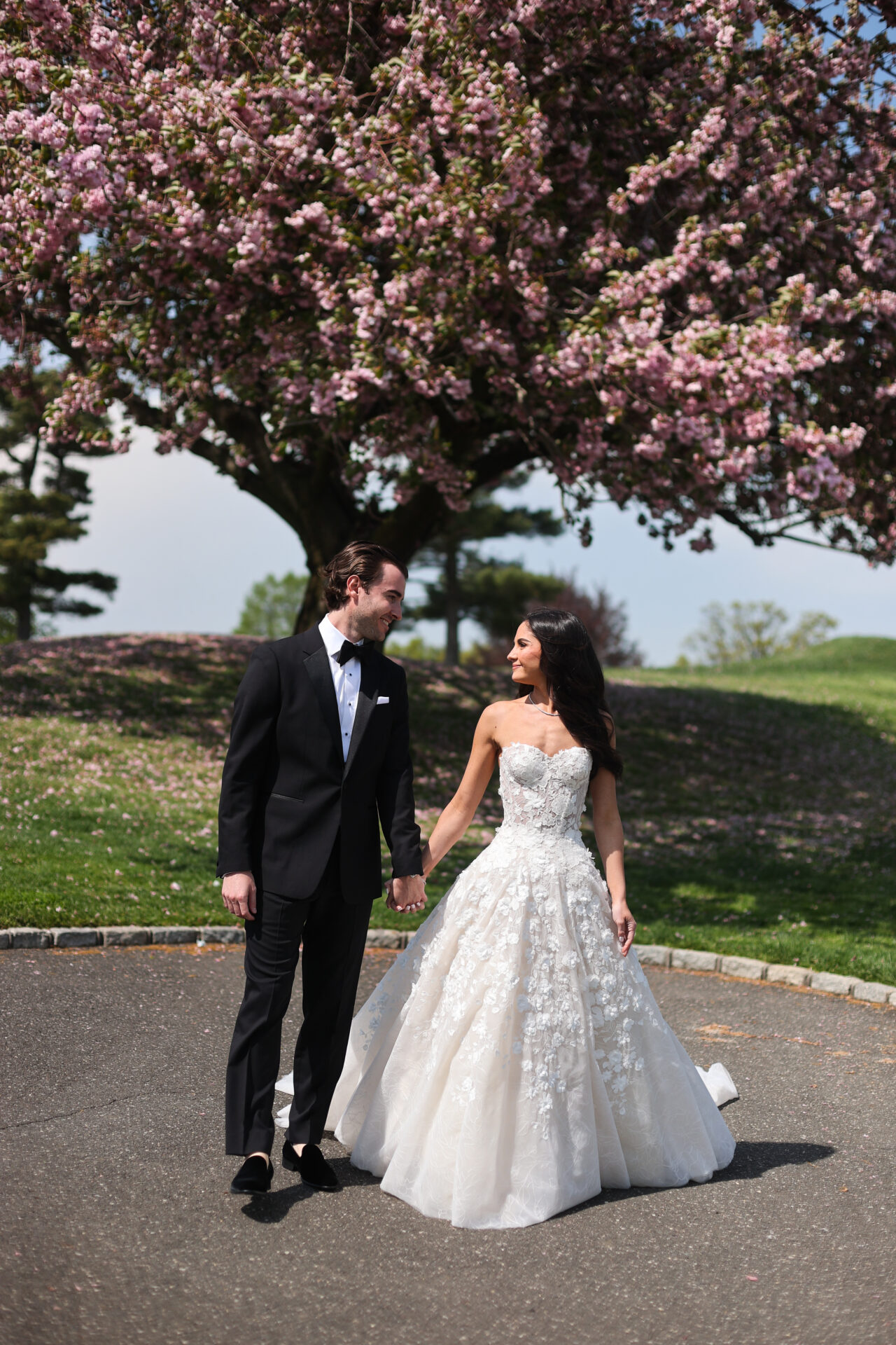 Bride and groom smiling under blooming cherry blossoms.