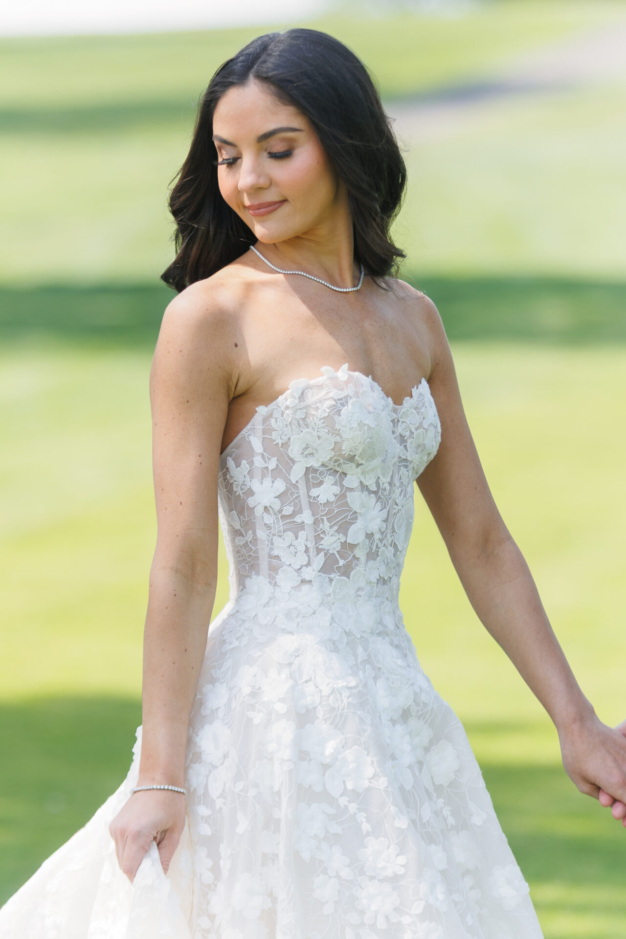 Woman in floral lace wedding dress smiles outdoors.