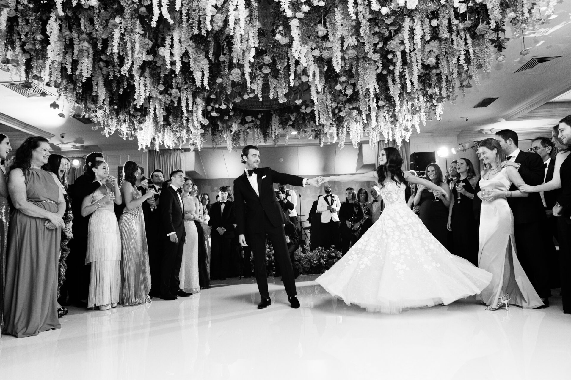 Bride and groom’s first dance; smiling guests watch.