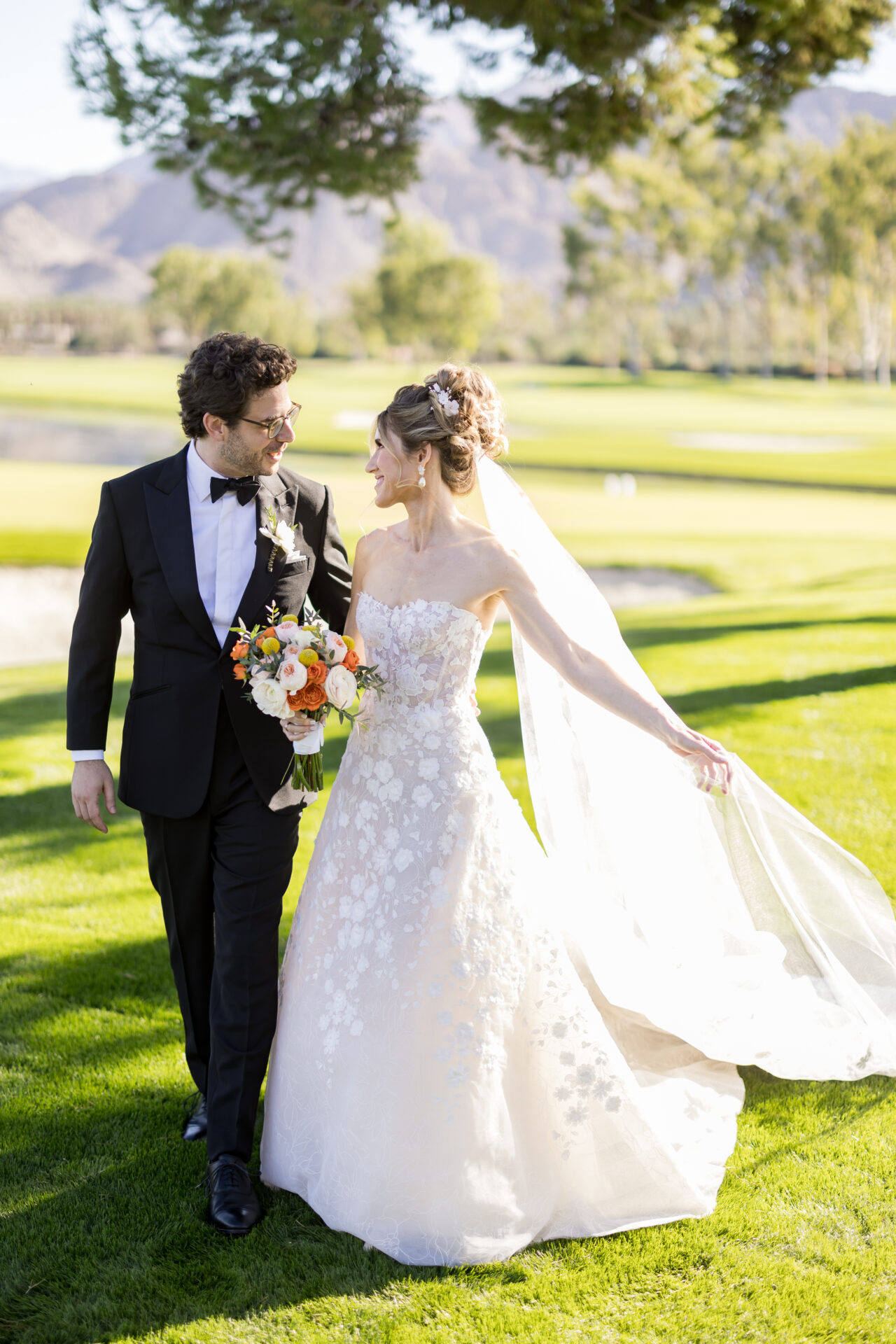 Bride and groom walk hand in hand outside smiling.