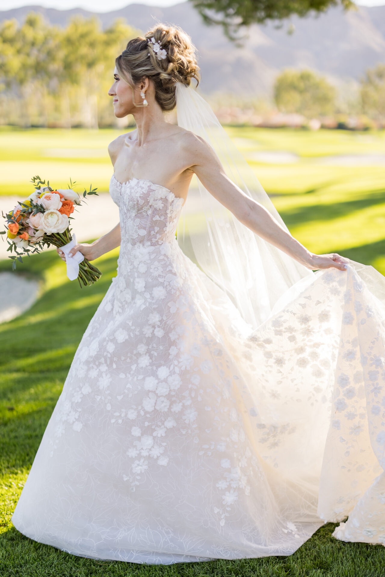 Bride in lace gown and veil, holding bouquet outdoors.
