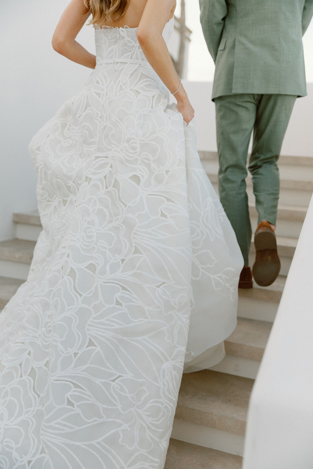 Bride and man ascend stairs; gown trails behind.
