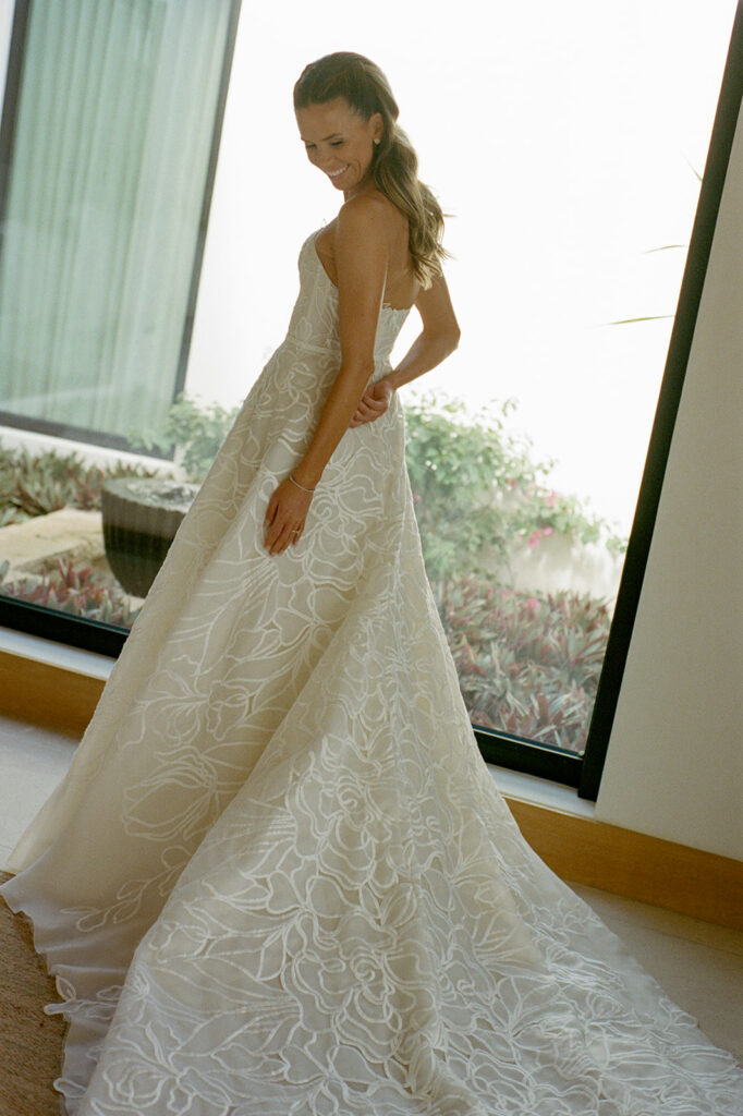 Woman in floral wedding dress smiles, sunlight behind.