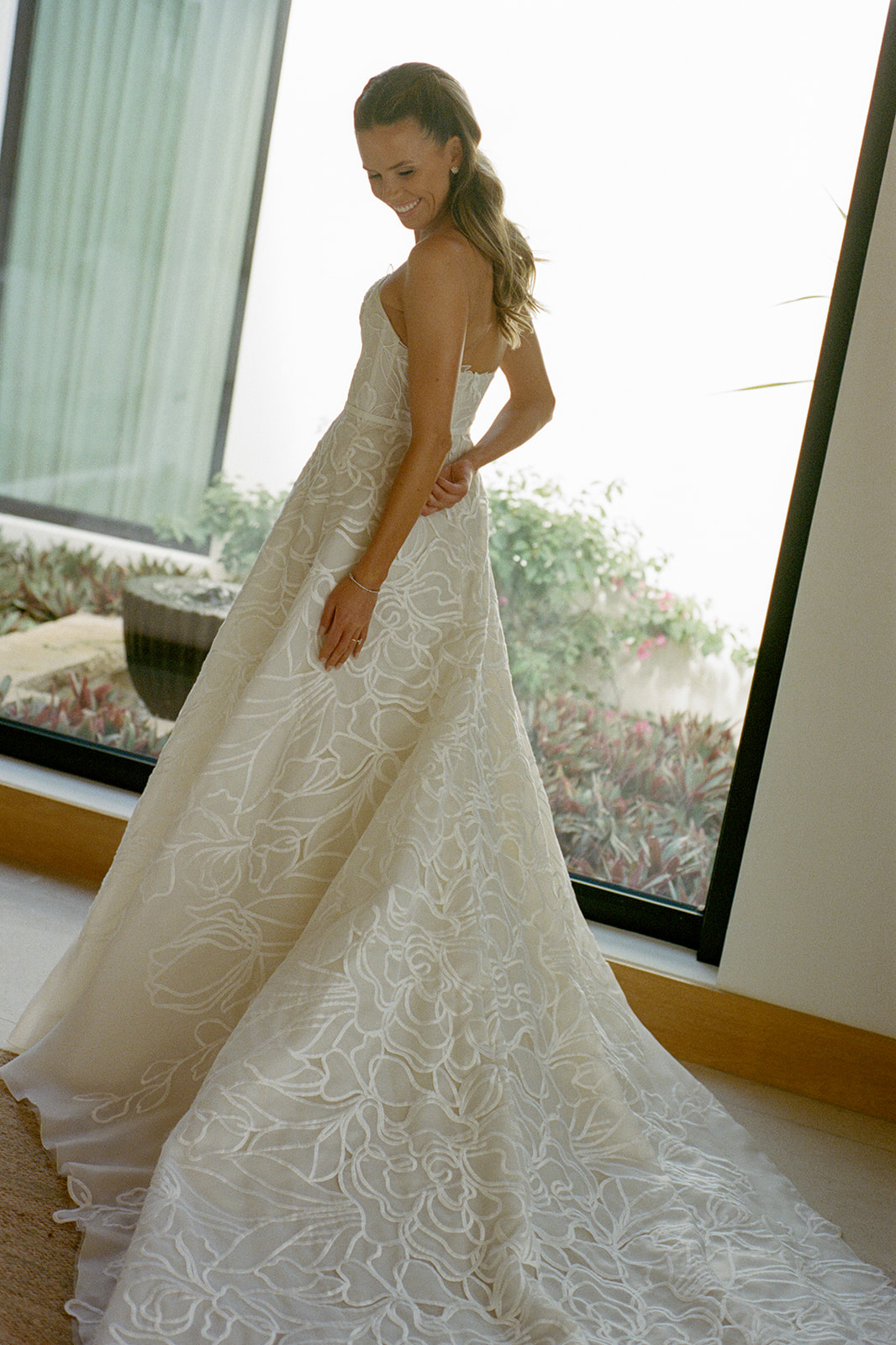Woman in floral wedding dress smiles, sunlight behind.