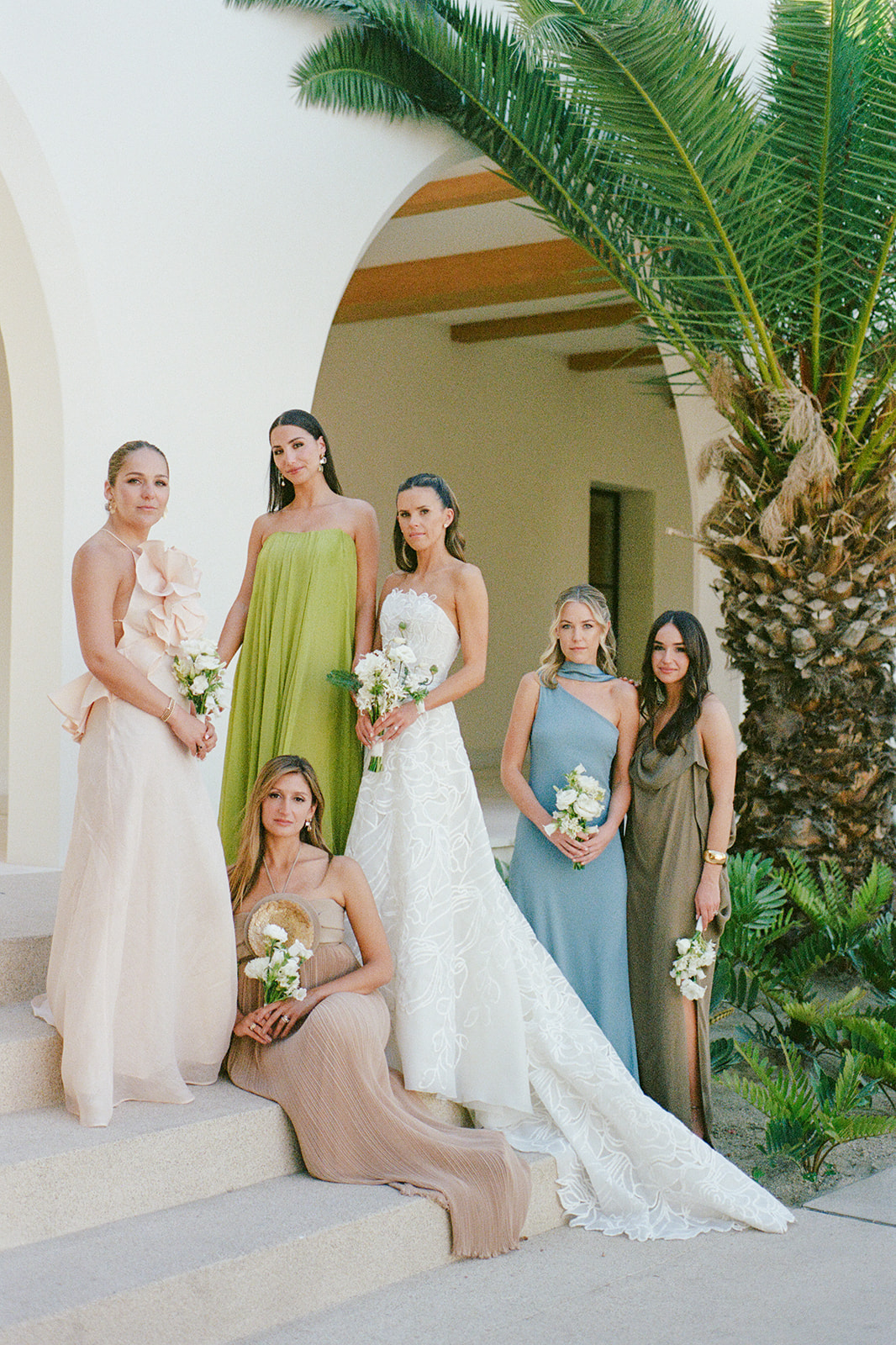 Bride with five bridesmaids pose on steps, holding bouquets.