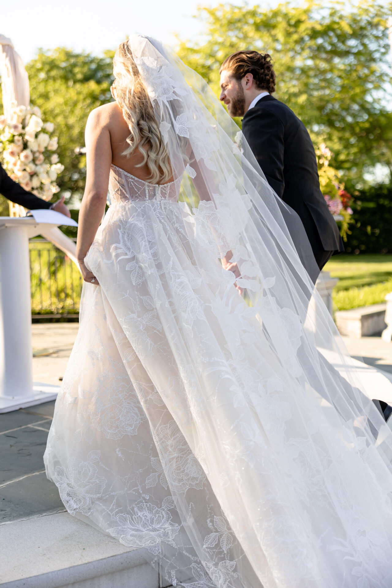 Bride in lace gown ascends steps; groom beside her.