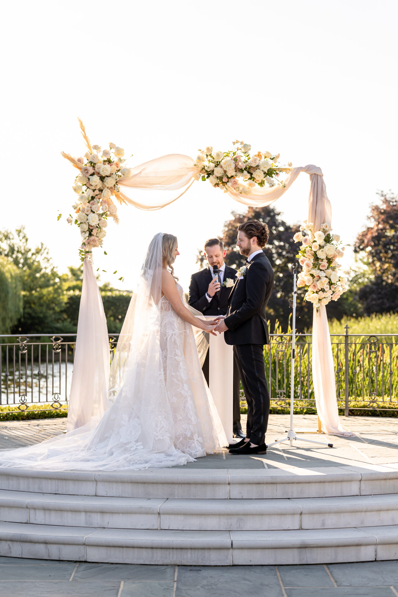 Bride and groom hold hands under floral arch outdoors.