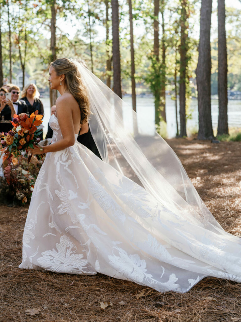 Katya Ruiz outdoors in couture gown, orange bouquet, veil flowing.