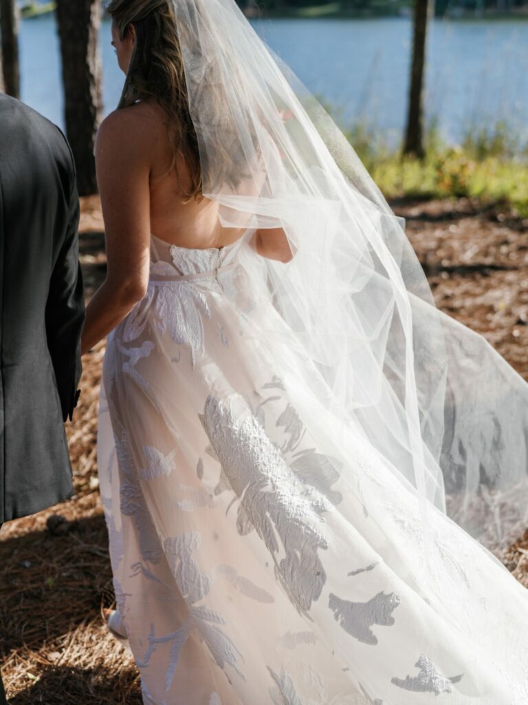 Bride Katya Ruiz in floral gown, lakeside with companion.