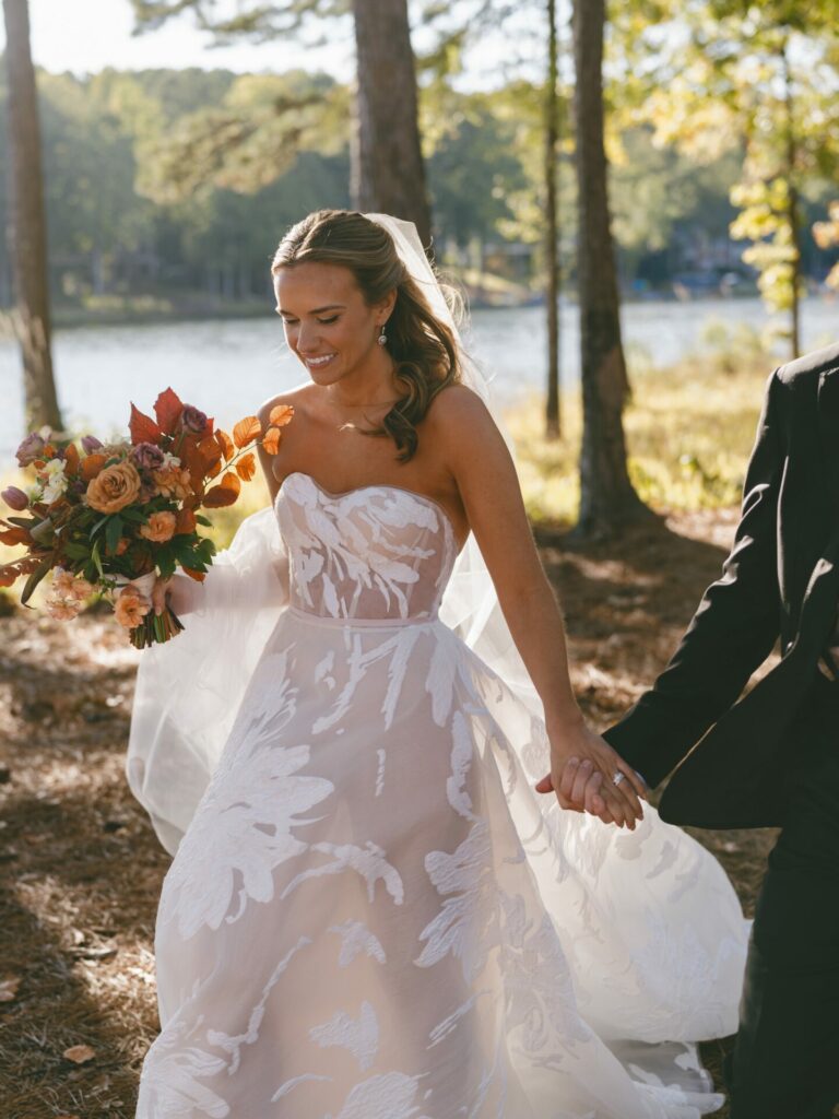 Katya Ruiz in bridal gown by a lake, hand-in-hand.