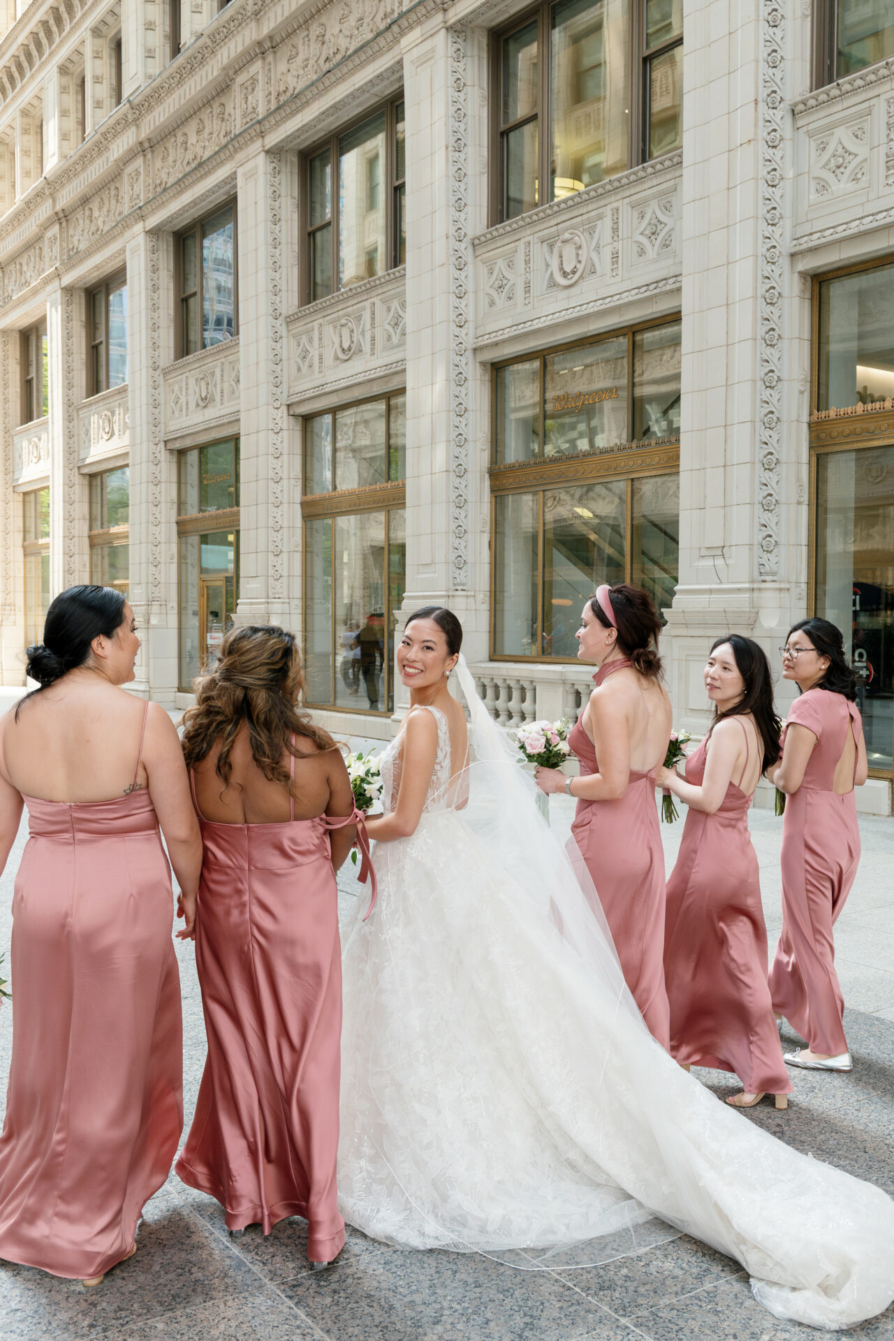 Bride with bridesmaids in pink dresses outside building.