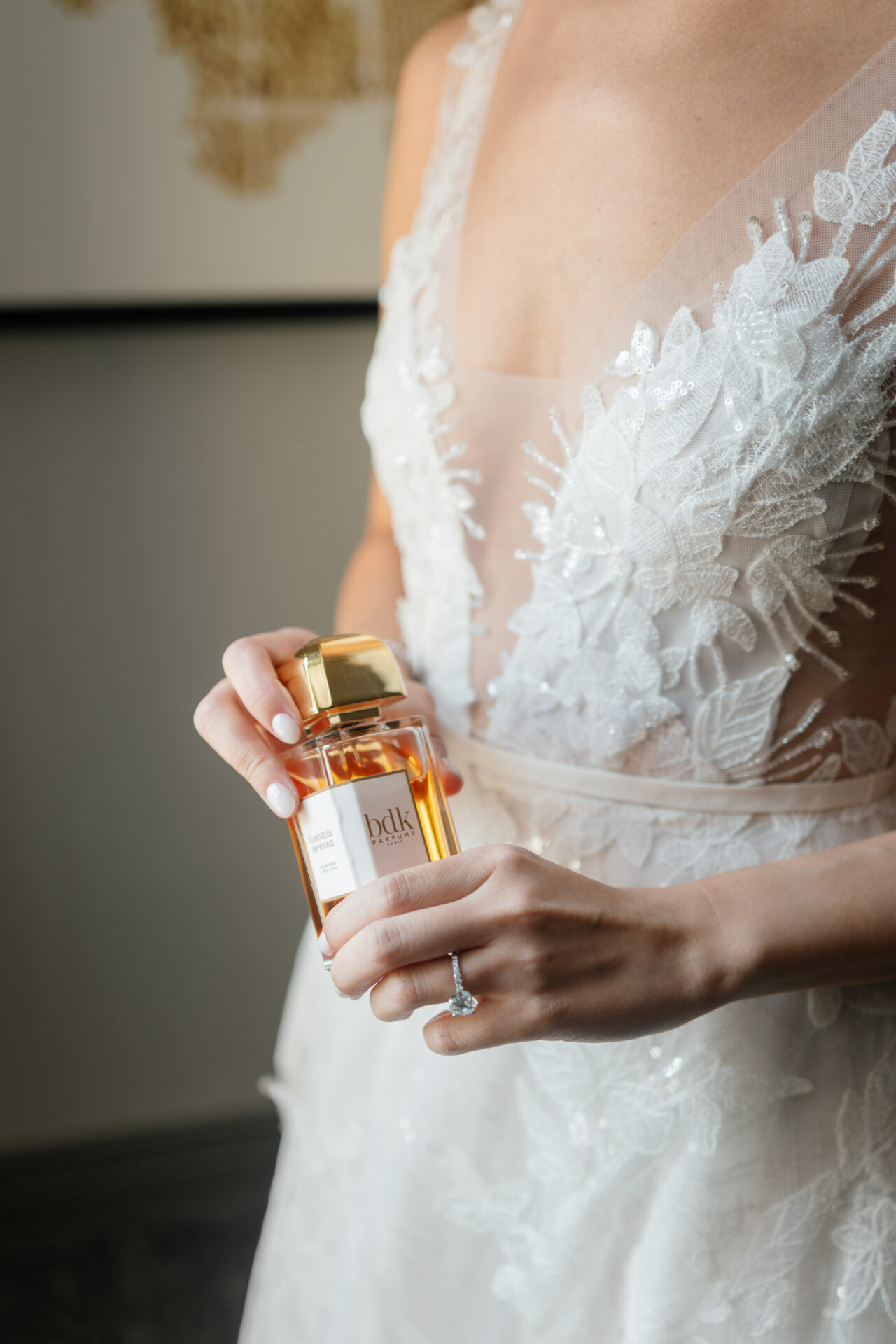 Bride in embroidered dress displays perfume and ring.