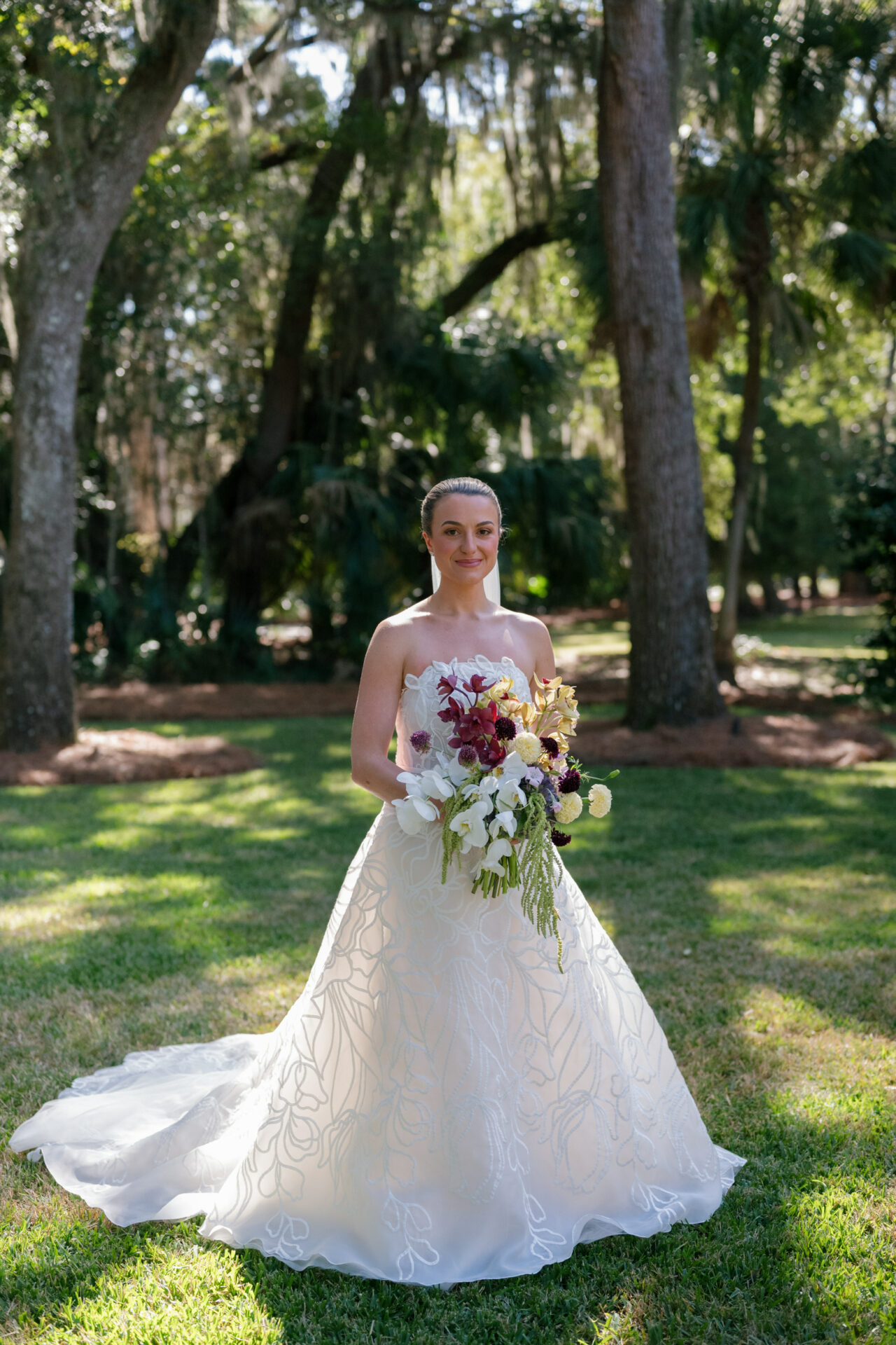 Bride in white gown with bouquet on sunny lawn.