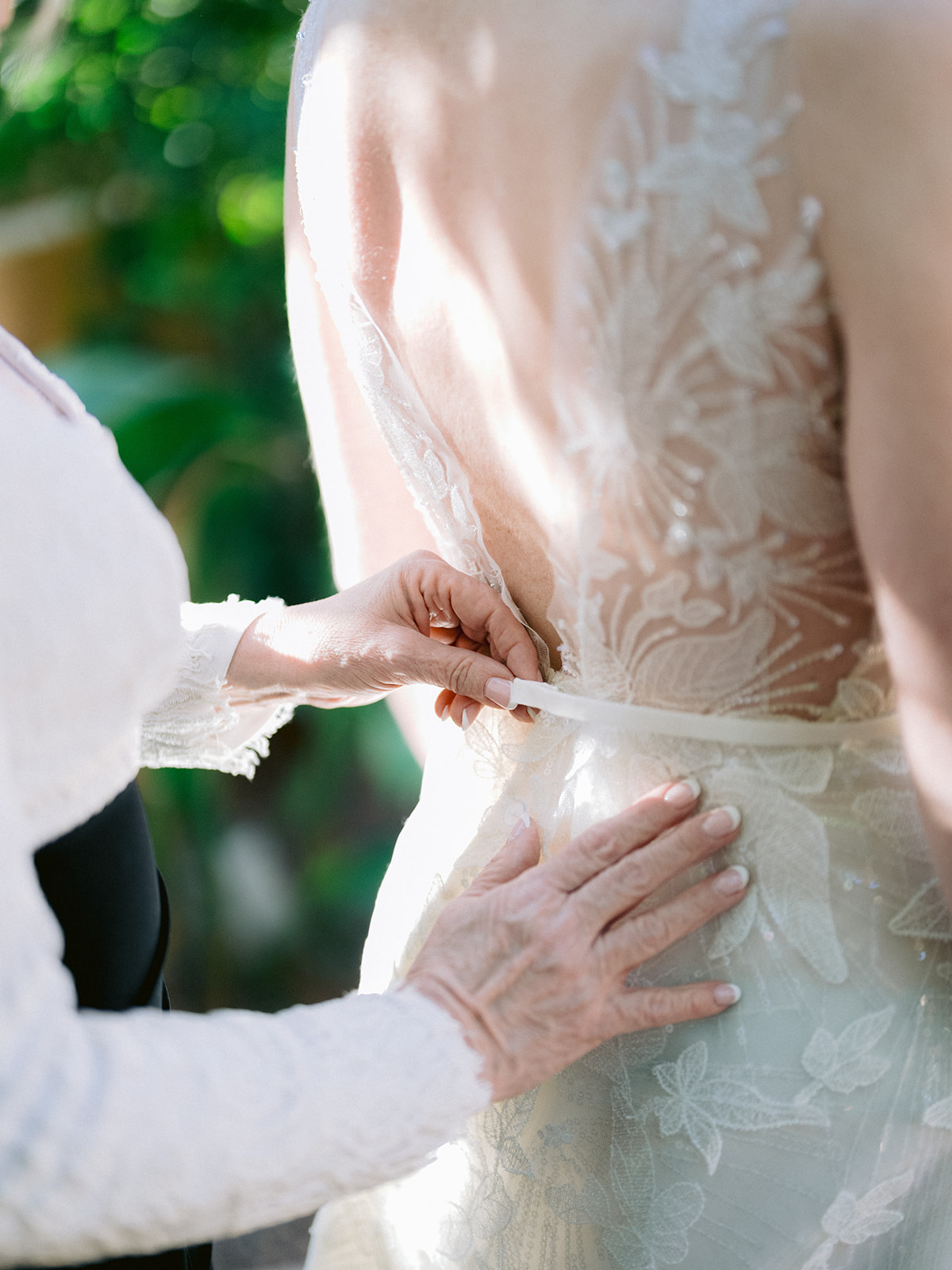 Hands zip up white lace dress in sunlight.