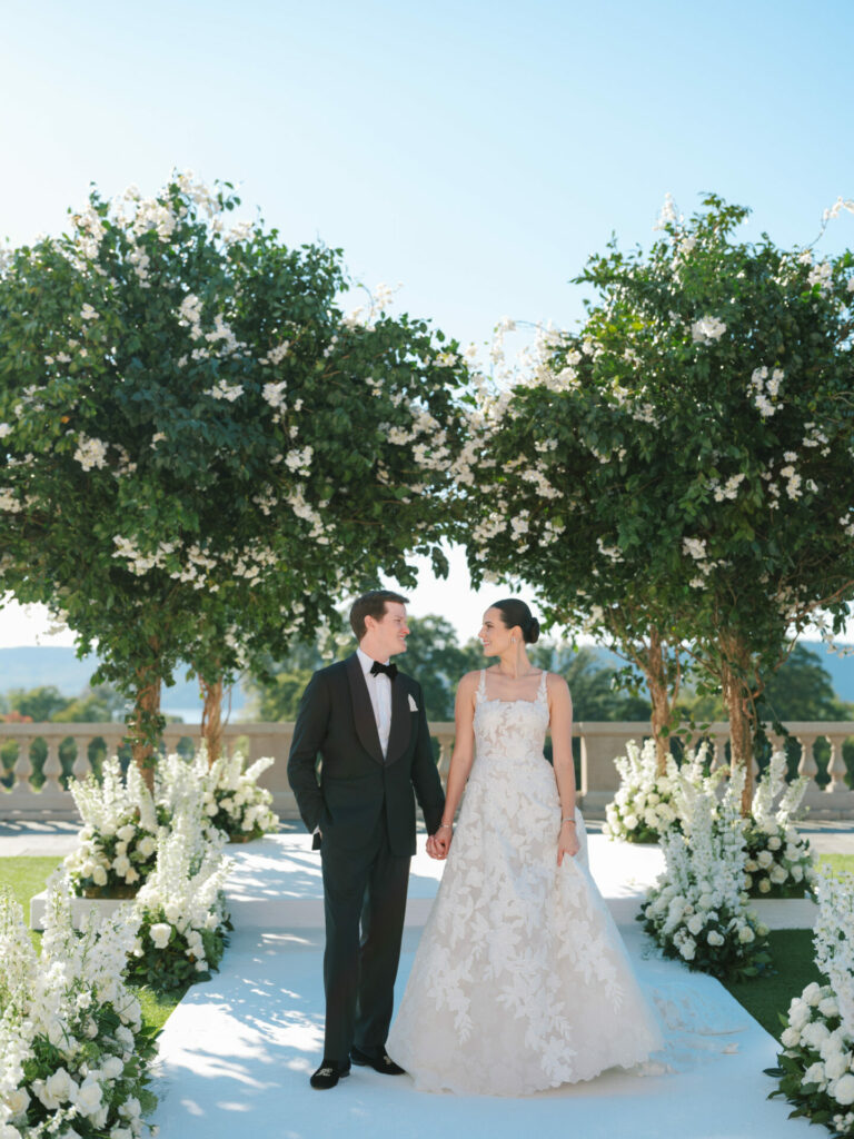 Katya Ruiz in couture gown, hand-in-hand with groom outdoors.