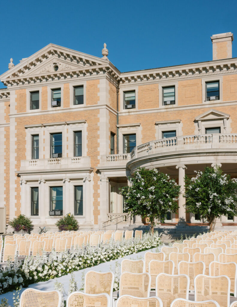 White chairs and aisle flowers before a grand building.