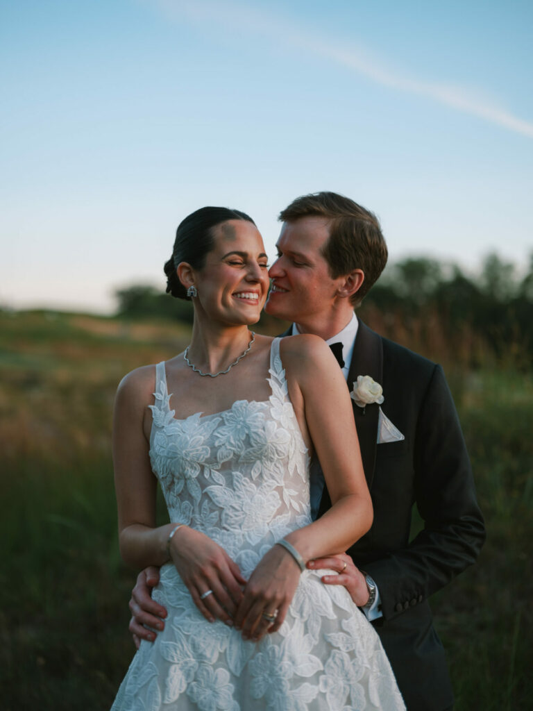 Bride and groom embrace at sunset in luxury attire.