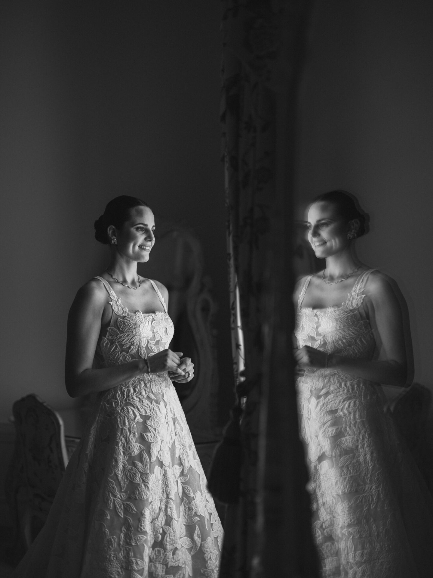 Bride in luxury gown smiles at mirror, reflected.