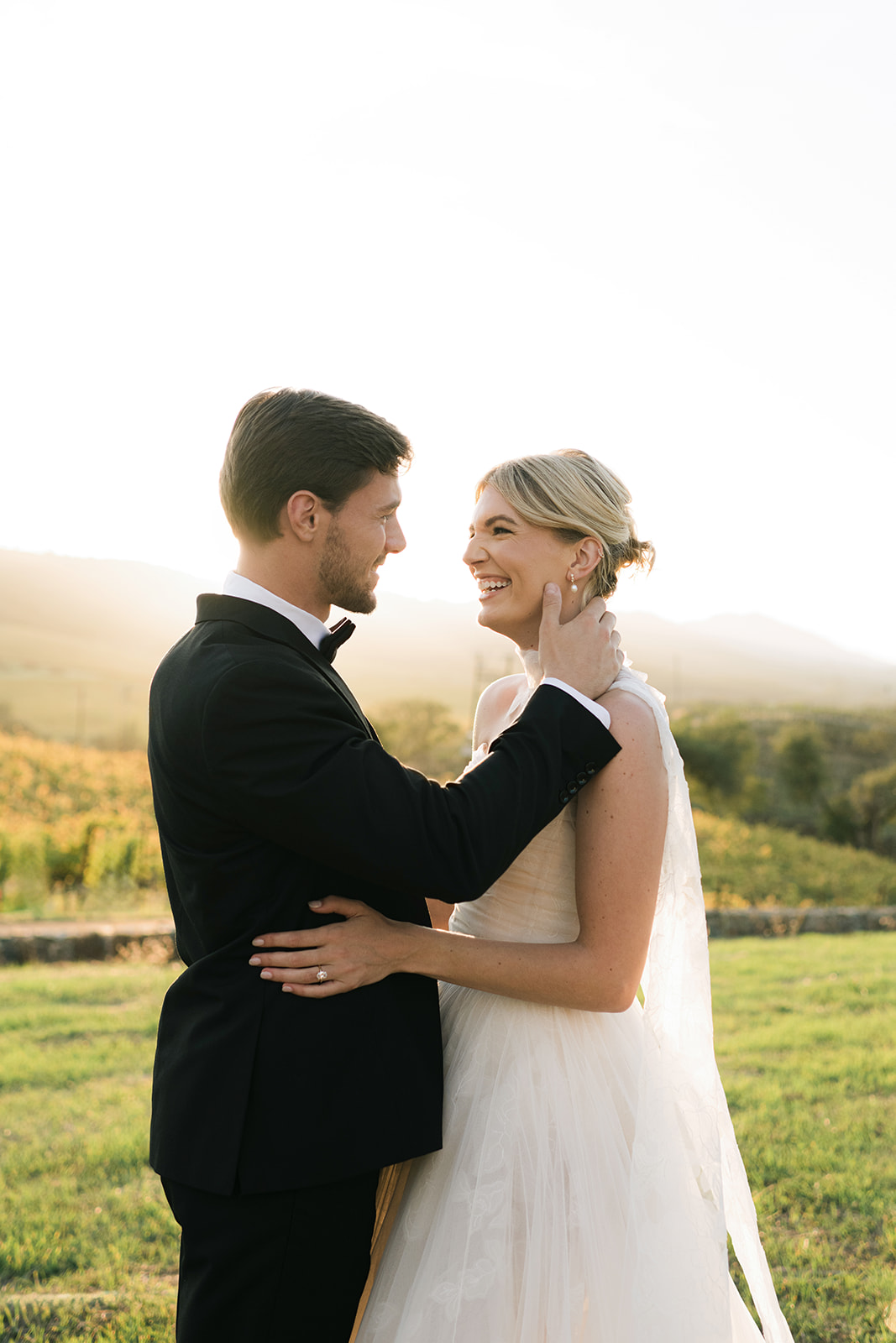 Bride and groom smile at sunset, formal attire.