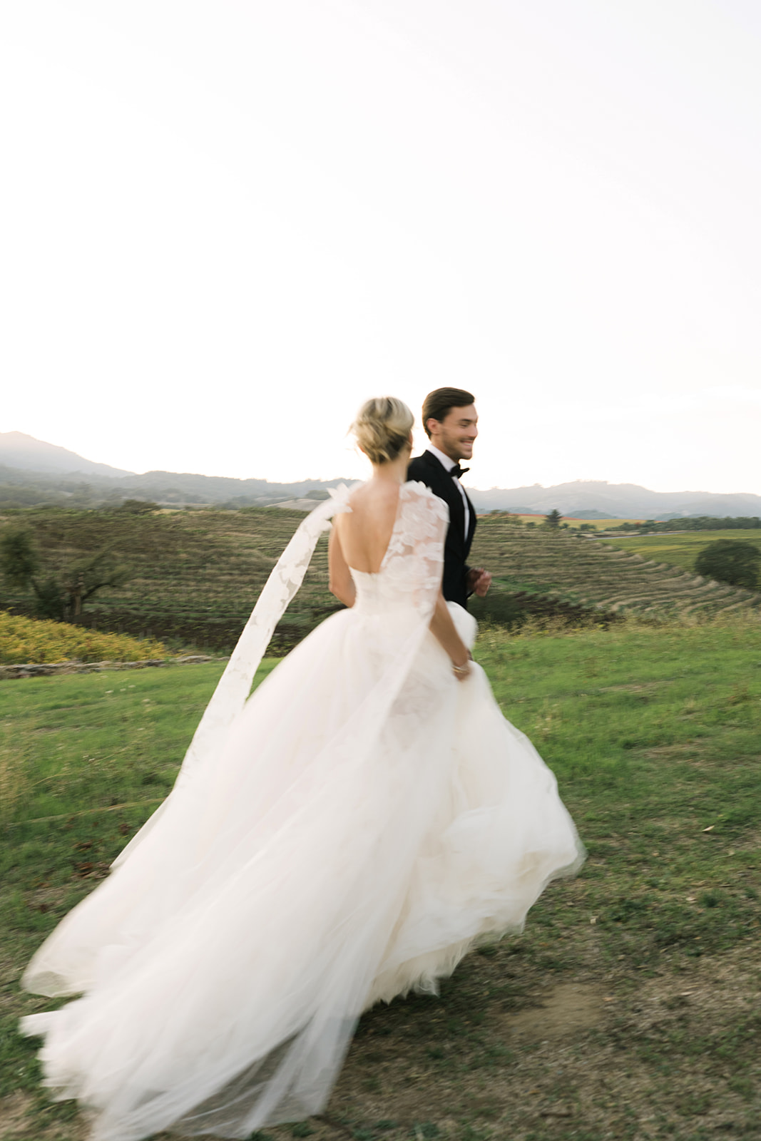 Bride and groom walk hand in hand outdoors.