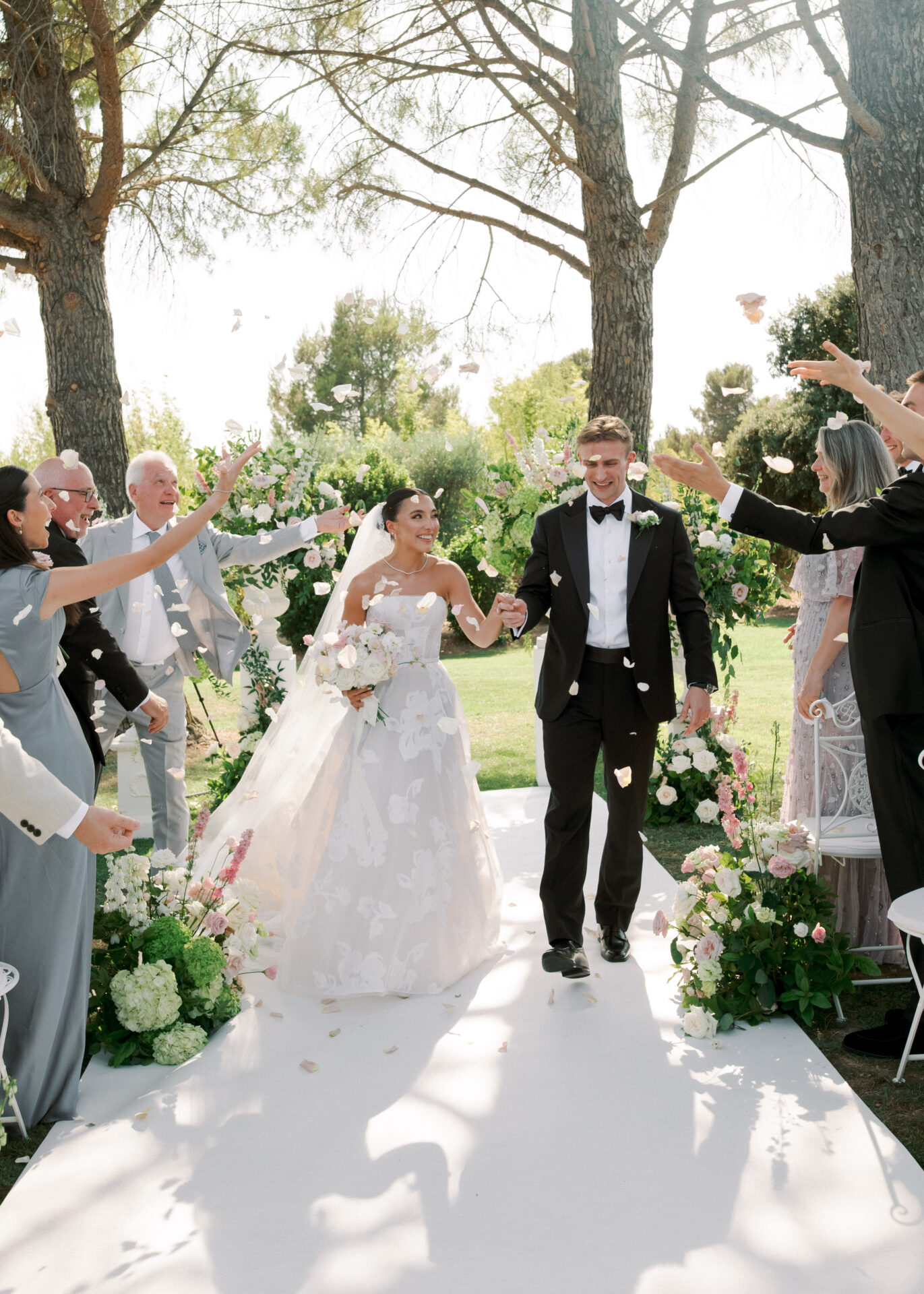 Bride and groom walk aisle as guests toss petals.