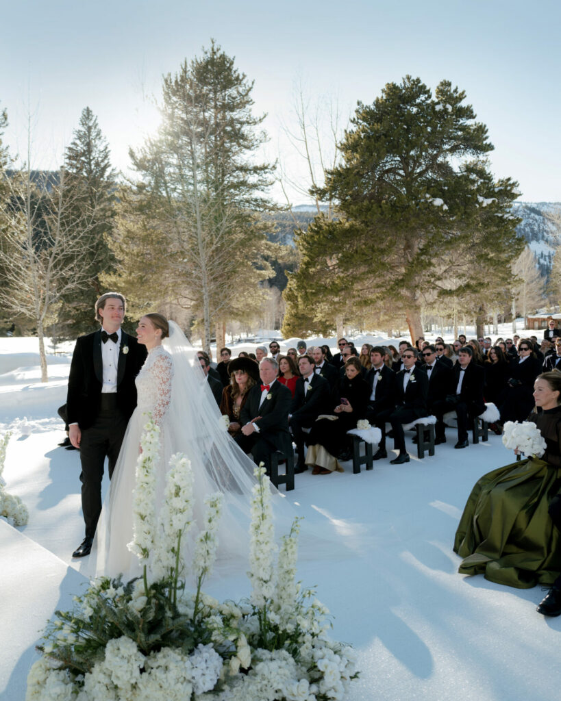 Bride and groom at snowy outdoor wedding among trees.