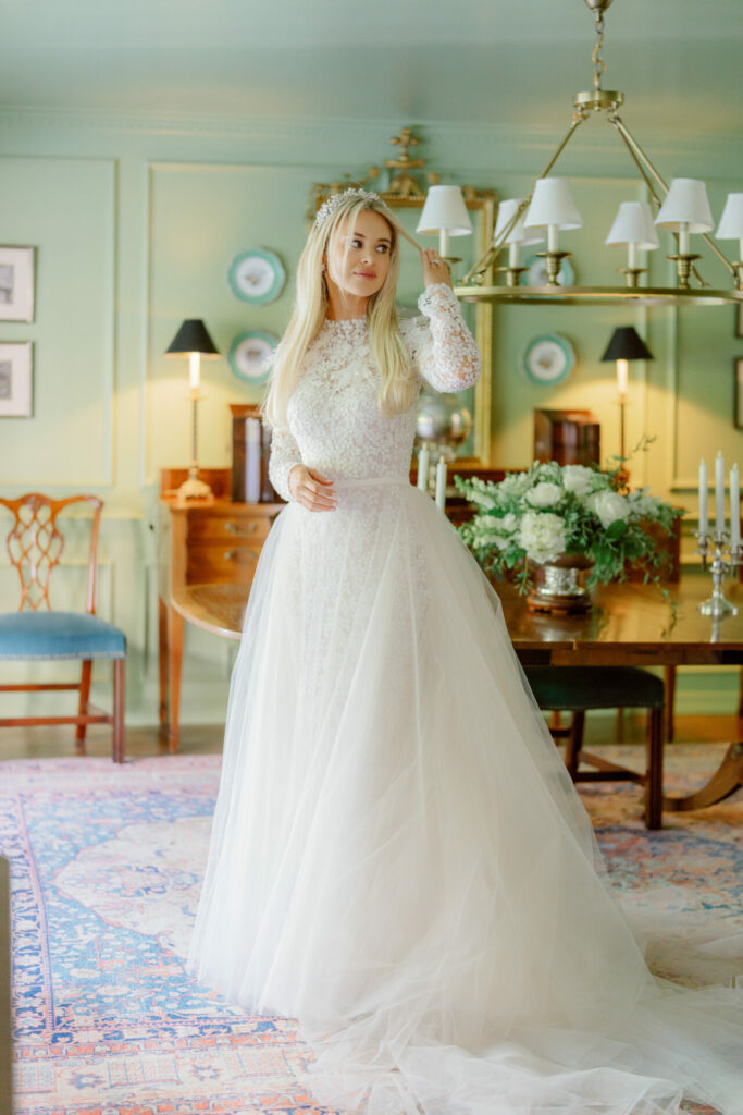 Bride in lace gown stands in elegant, antique room.