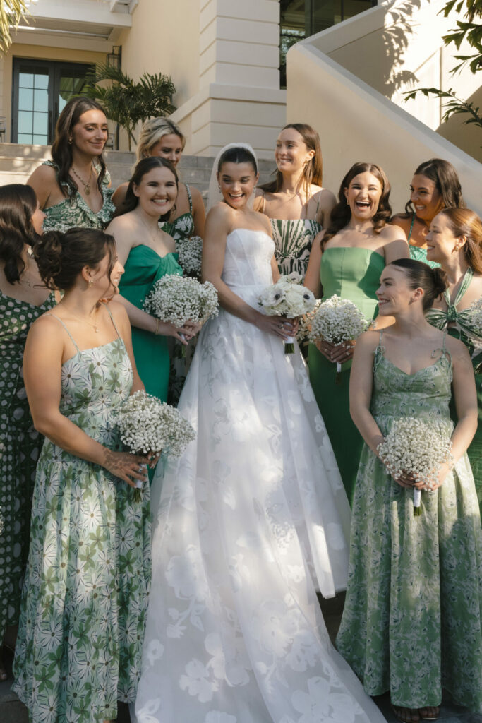 Bride in white gown with smiling bridesmaids in green.