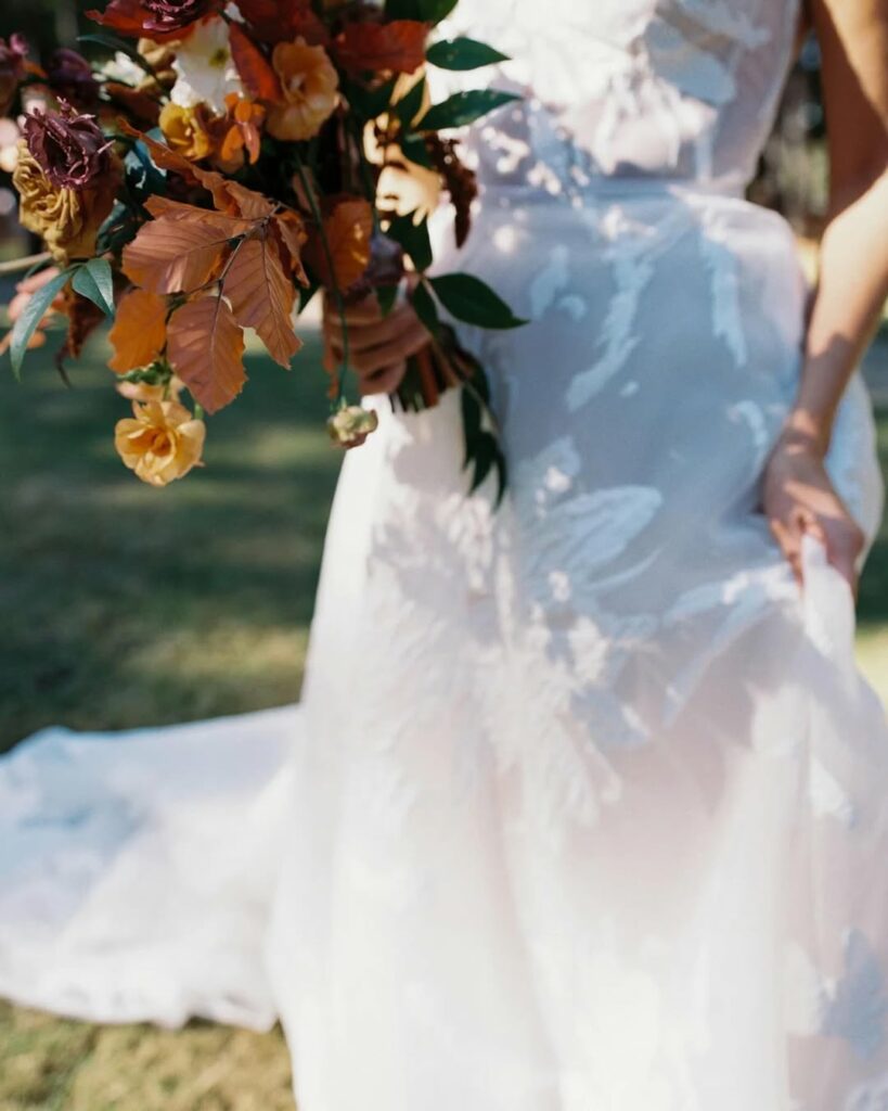 Person in floral wedding dress holding bouquet outdoors.