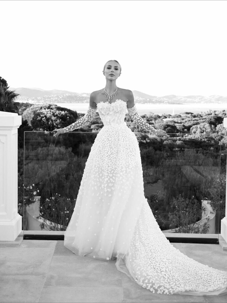 Woman in floral gown on terrace, scenic backdrop.