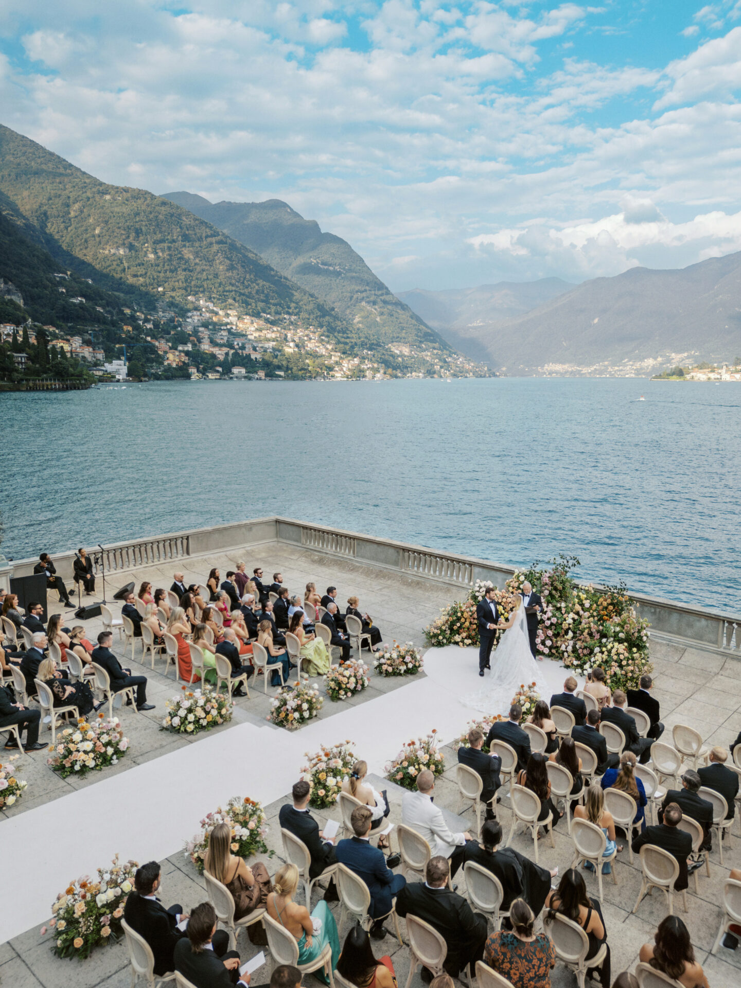 Lakeside wedding, mountain views, floral decor, guests seated.