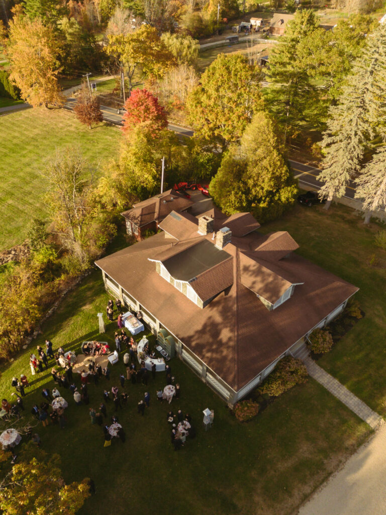 People gather outdoors by brown-roofed house in autumn.