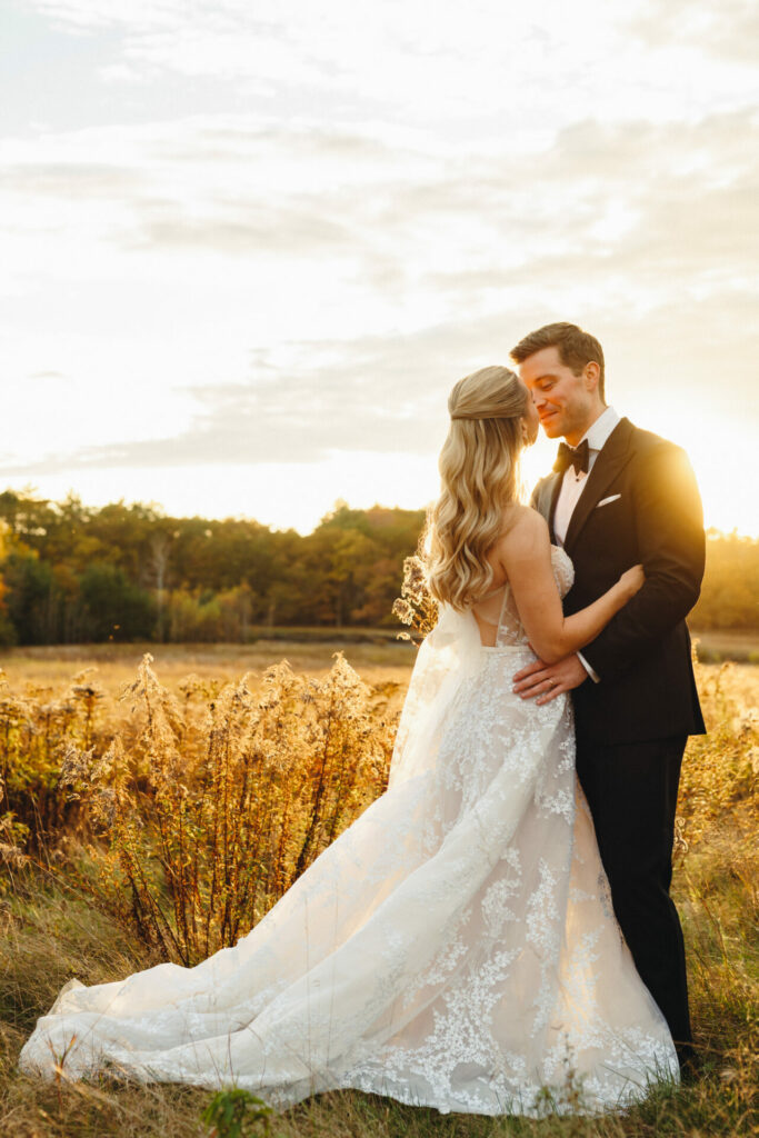 Bride and groom embrace in field at sunset.