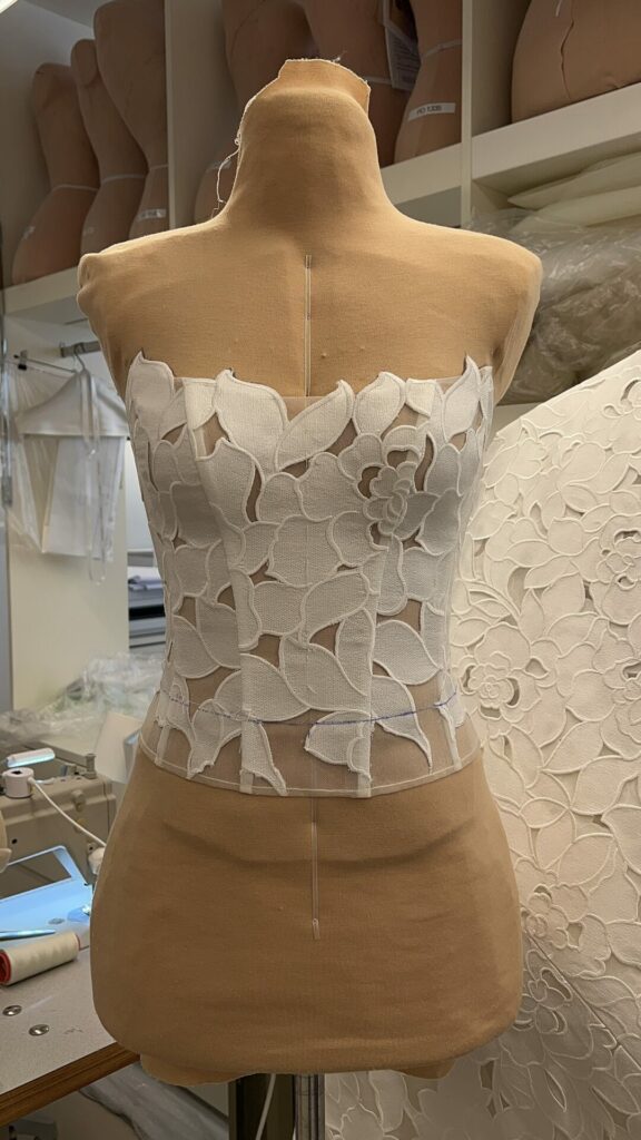 Mannequin wears floral white corset; matching fabric nearby.