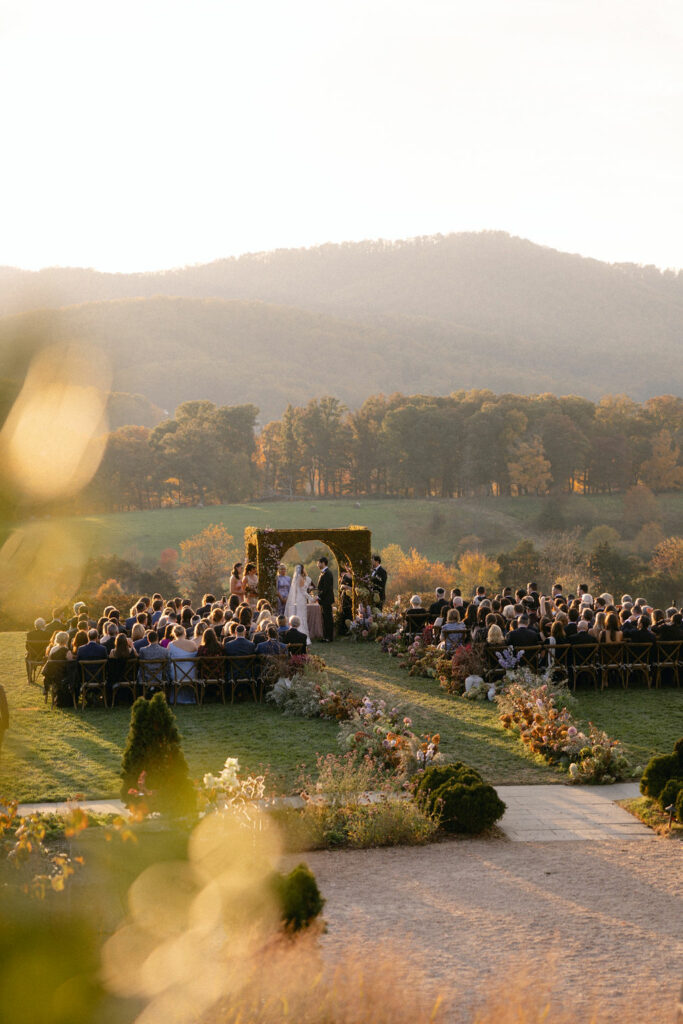 Sunset wedding, floral aisle, arch, hills, guests gathered.