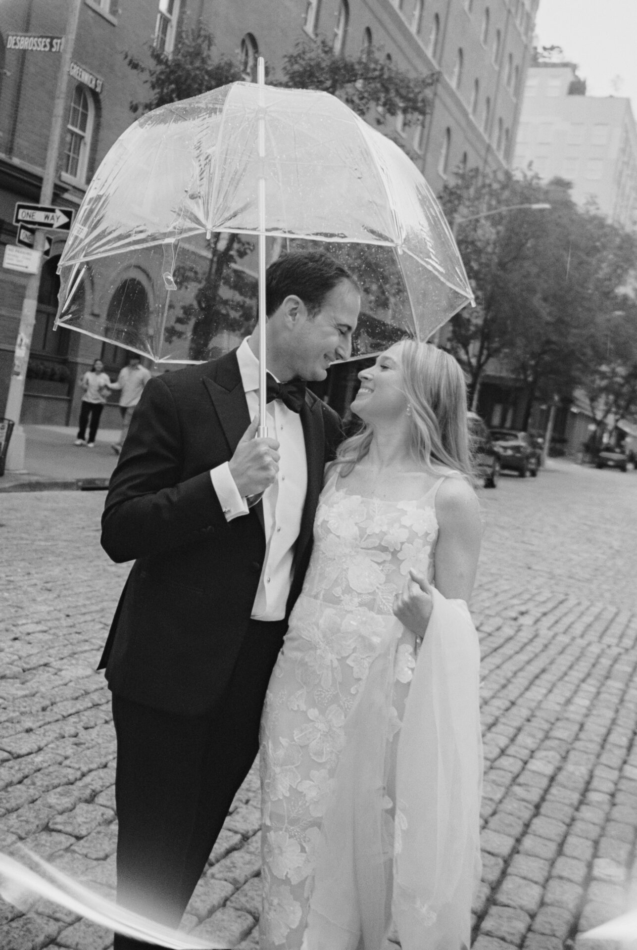 Smiling couple under umbrella in formalwear, black-and-white.