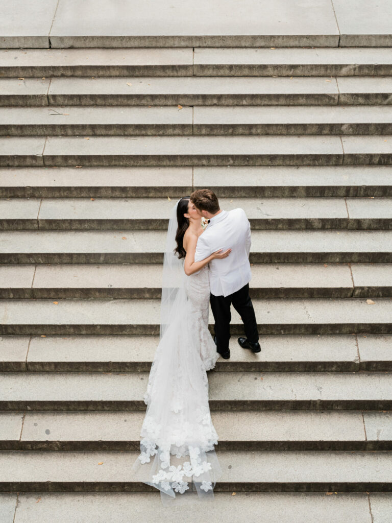 Bride kisses groom on stone steps, viewed above.