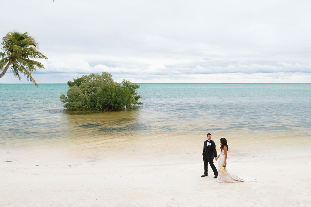 Bride and groom stroll beach, turquoise sea, "Far Beyond.