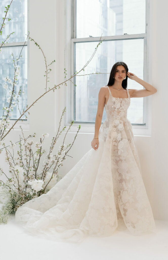 Woman in floral white gown by bright window.