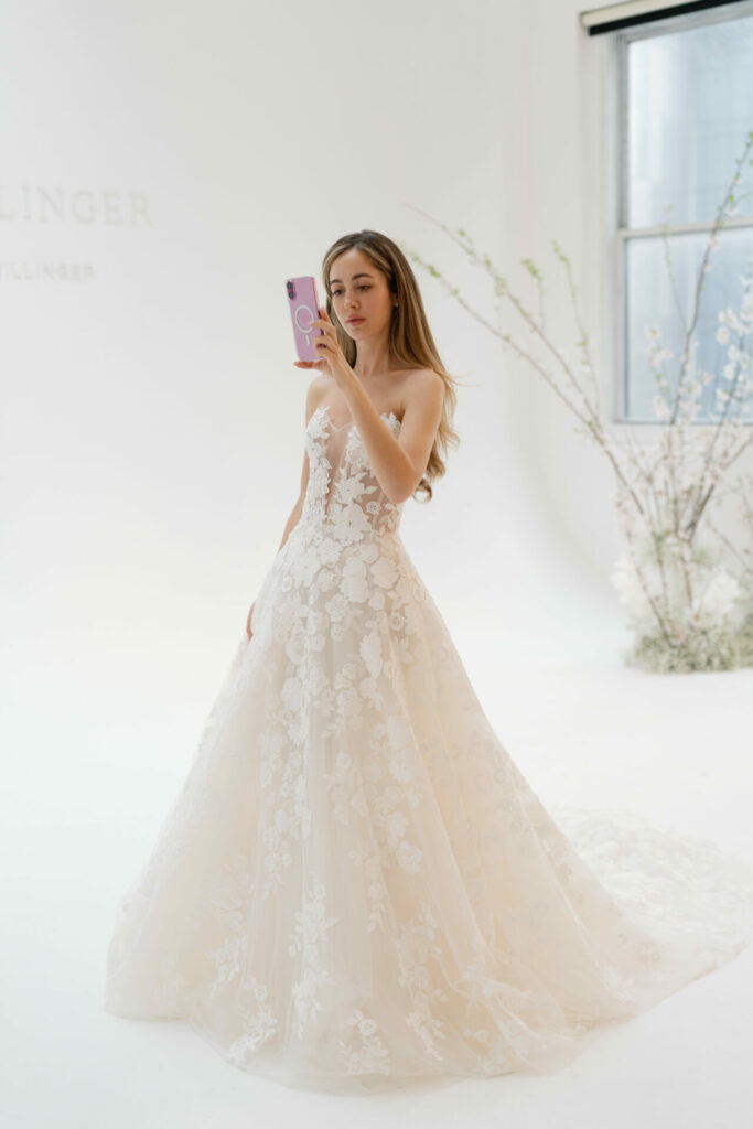 Woman in floral lace wedding dress takes selfie.