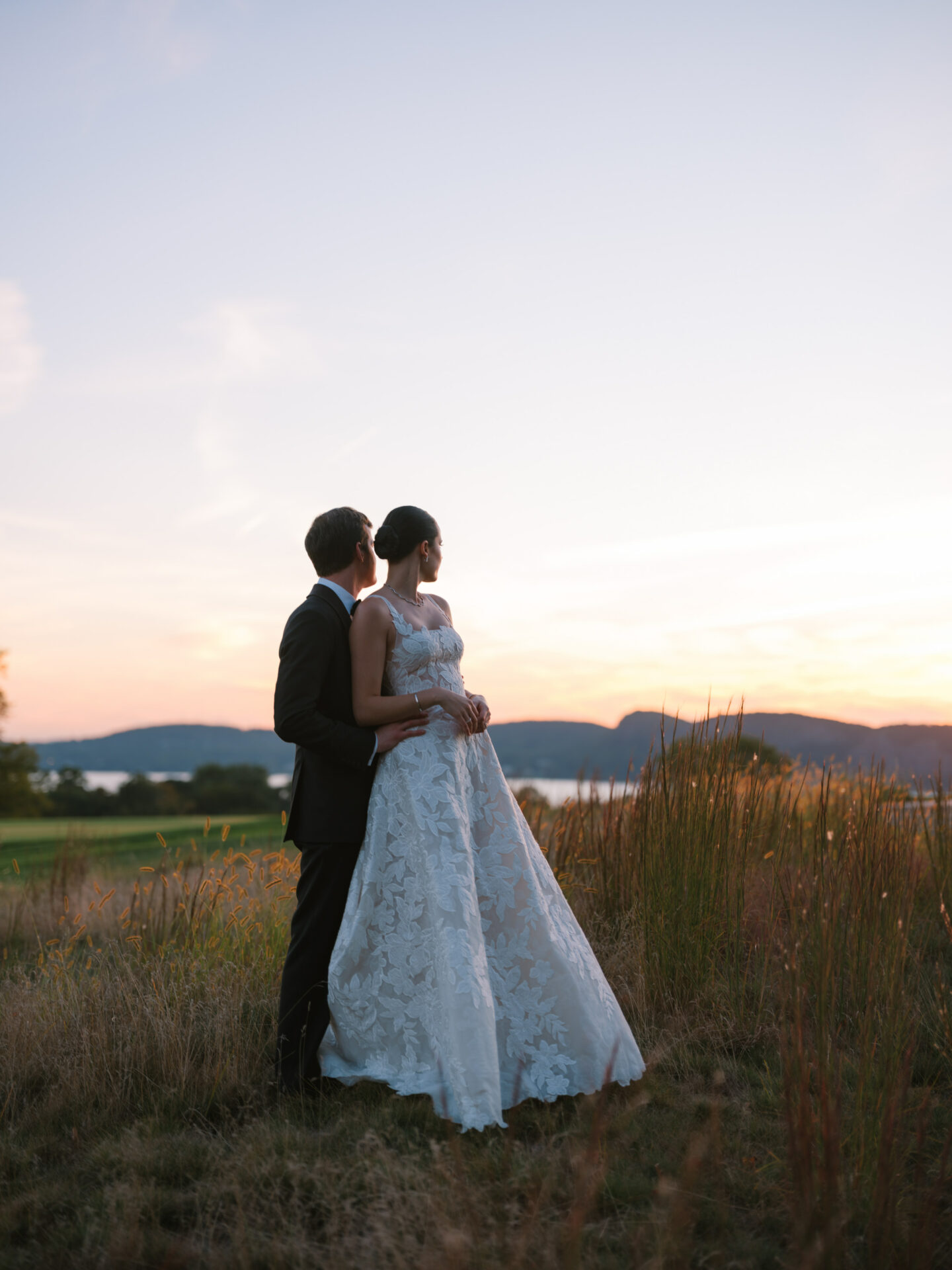 Bride and groom in tall grass at sunset.