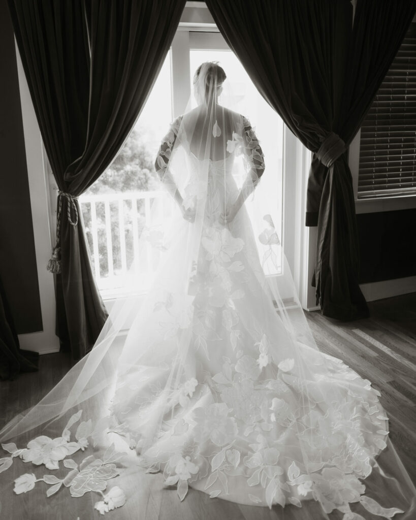 Bride in floral SS2026 gown, backlit by window.