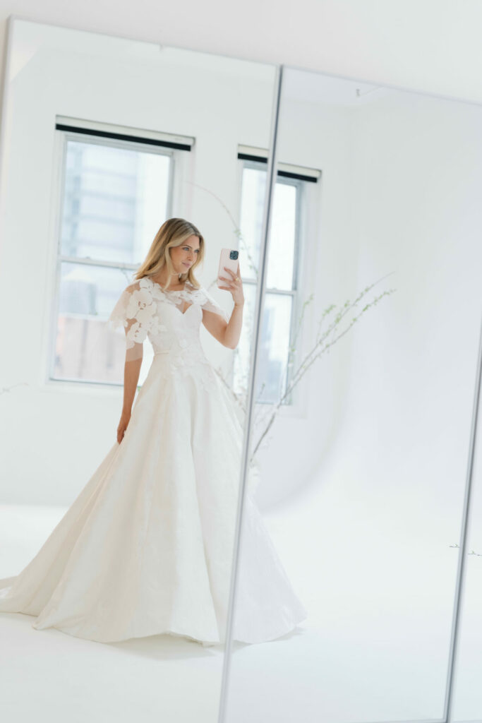 Bride in floral wedding dress takes mirror selfie.