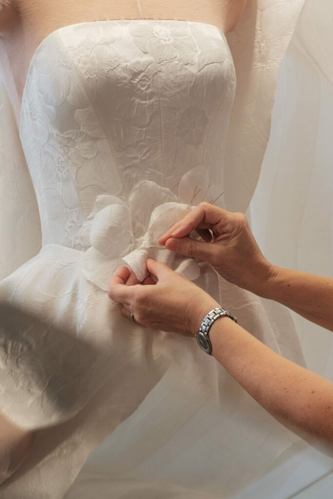 Hands adjust floral waist detail on strapless wedding dress.