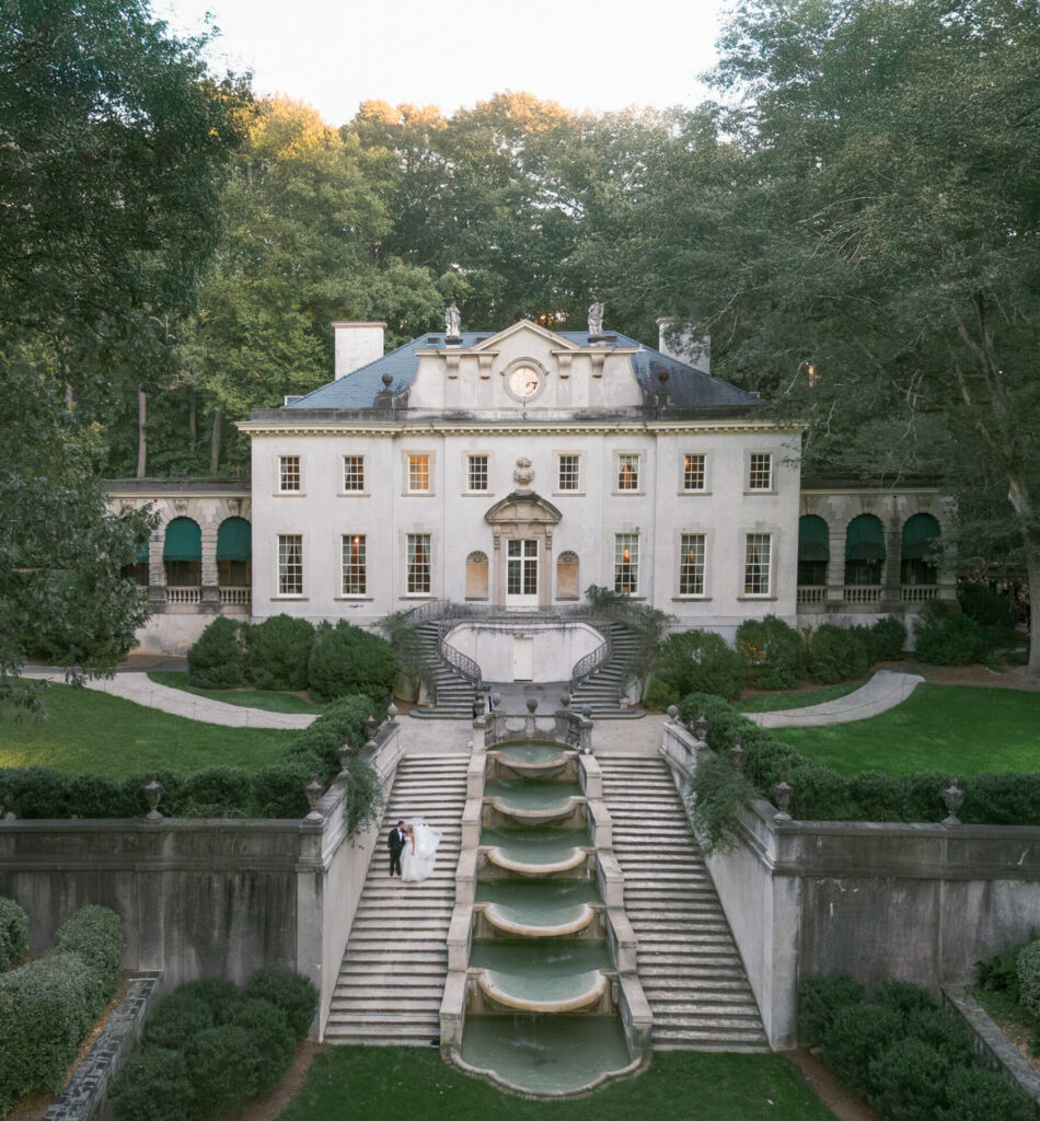 White mansion, fountain, trees; two people on steps.