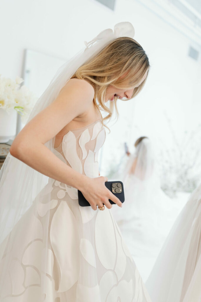 Smiling bride in white floral dress holding smartphone.