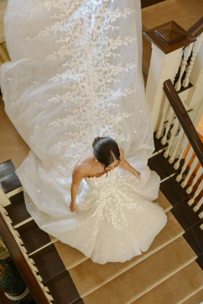 Bride ascends stairs in white gown with lace train.